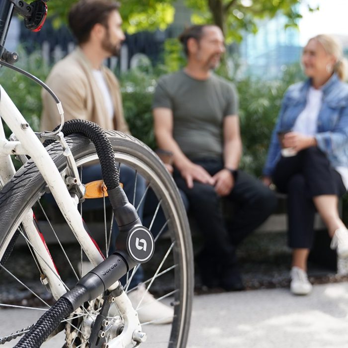 Op de achtergrond zitten drie mensen op een bankje. Vooraan staat een afgesloten fiets met het Serea slot.