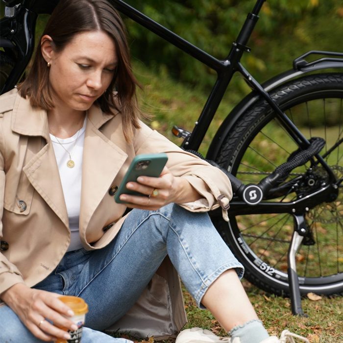Een vrouw kijkt op haar telefoon terwijl ze naast een fiets zit die is afgesloten met een zwart Serea-slot.
